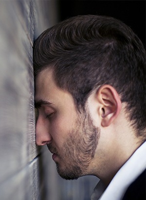 man closing eyes against a wall